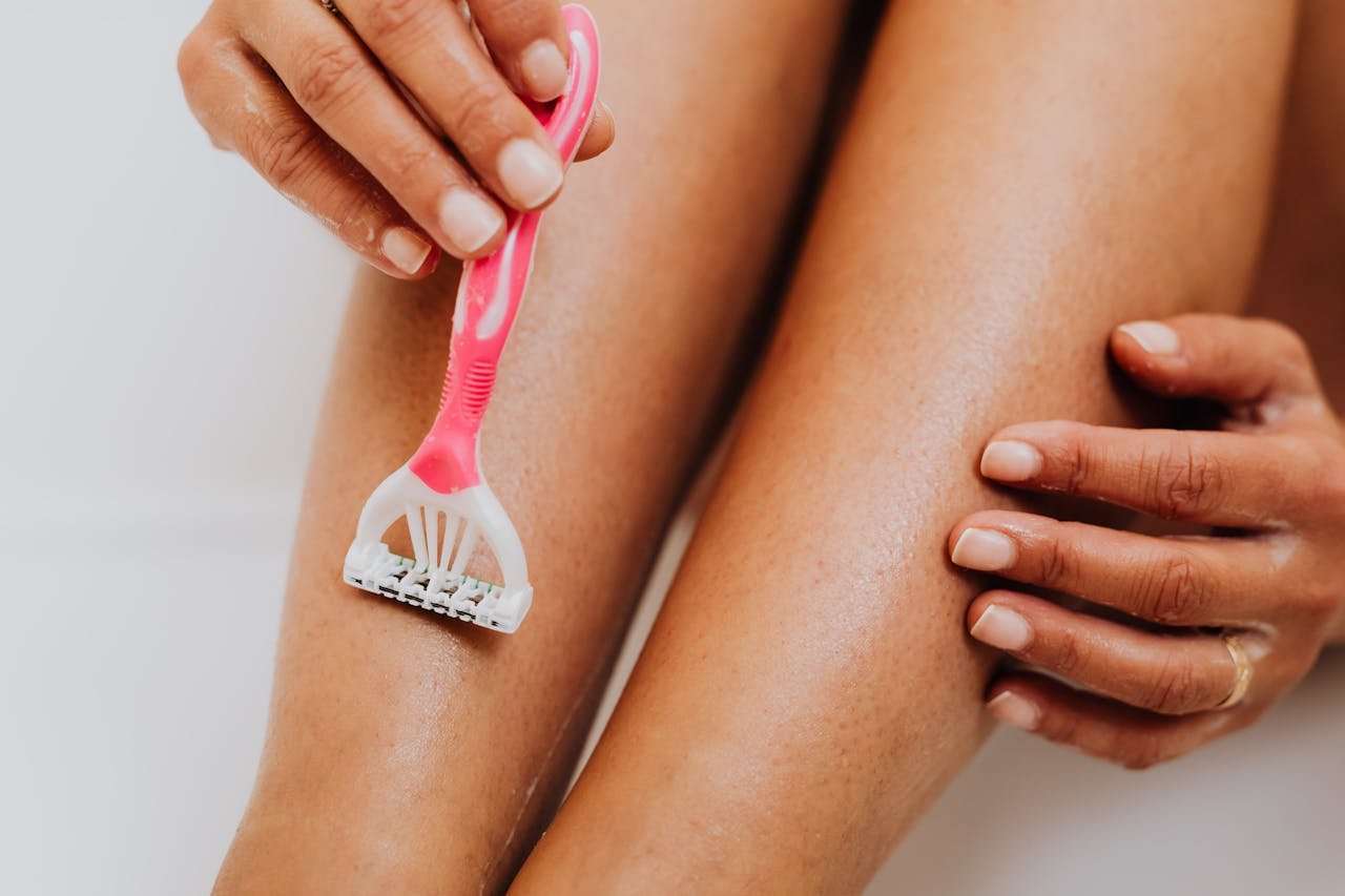 A close-up image of a person shaving their leg with a pink razor, focusing on smooth skin and personal care.