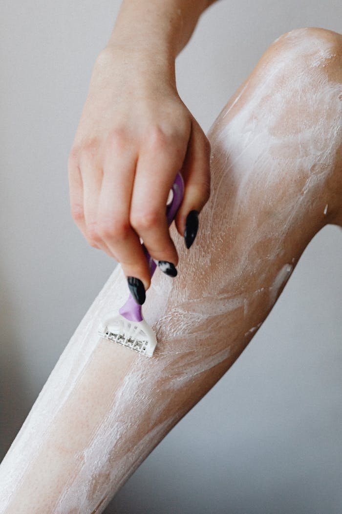 Close-up of a woman's hand using a razor to shave her legs with foam, depicting personal care.